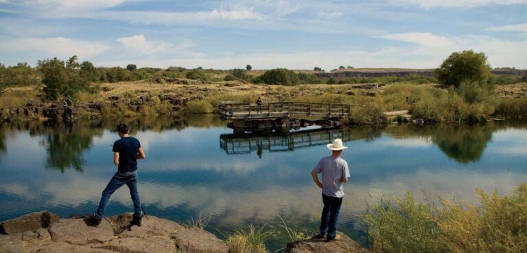Two men fish while standing on rocks before the calm waters of Oster Lake #1 in Hagerman, ID.
