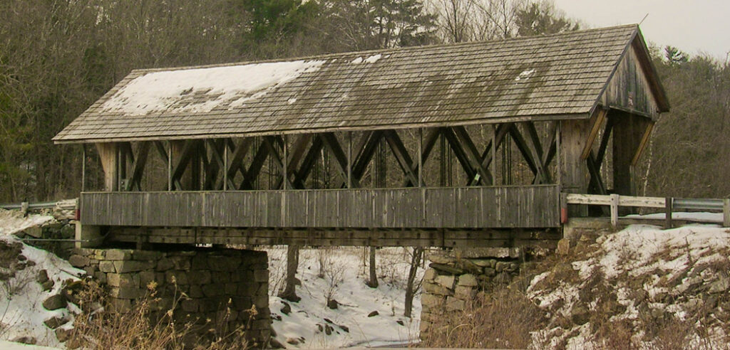 Snow covers the roof of this covered wooden bridge, Packard Hill Bridge spanning Mascoma River - Lebanon, NH