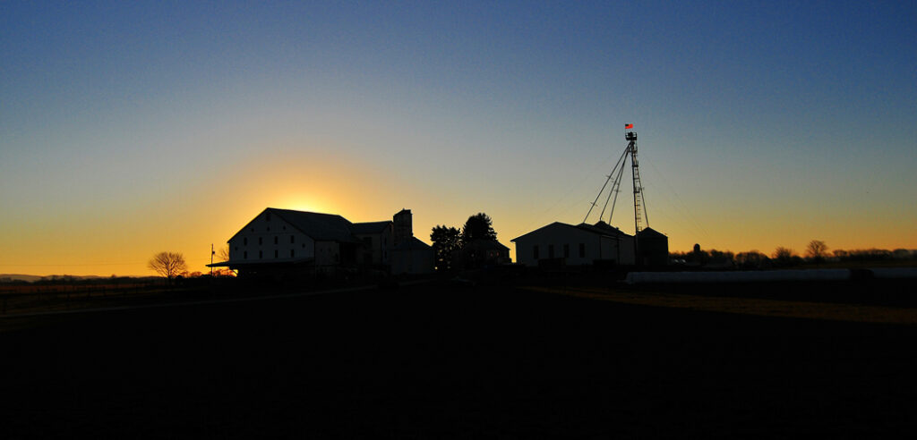 The sun drops behind a barn and silo putting them in shadows in Carlisle, PA