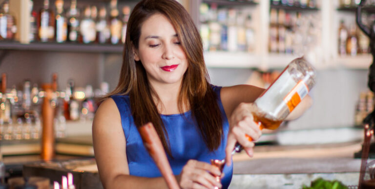 A female bartender in blue mixes a drink at Julep in Houston, TX.