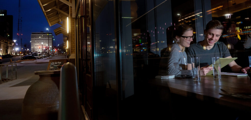 A couple sits near the window of The Grey Plume restaurant in Omaha, NE. They look at the menu.