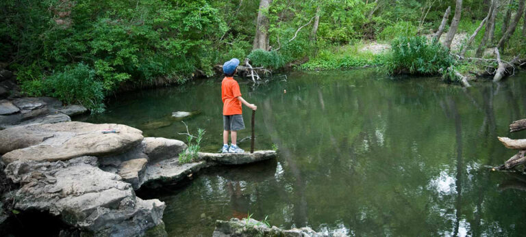 A boy in an orange shirt looks at the pond in Lockhart State Park, TX.
