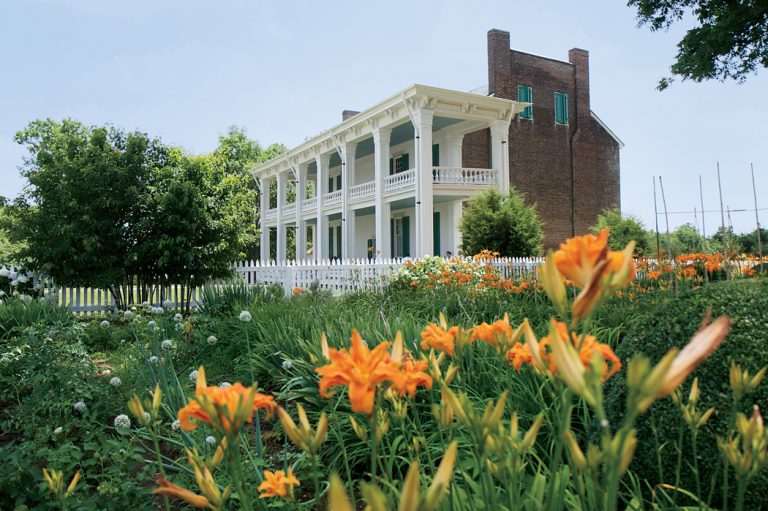 Yellow and orange flowers bloom in front of the historic Carnton Plantation home, a red brick building with large white columns.