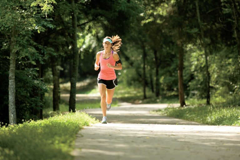A women in a pink shirt runs along a trail towards the camera in Deerwood Arboretum in Brentwood, TN.
