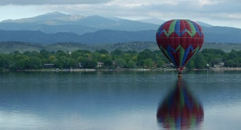 A colorful hot air balloon hovers just above the lake in Loveland, CO.