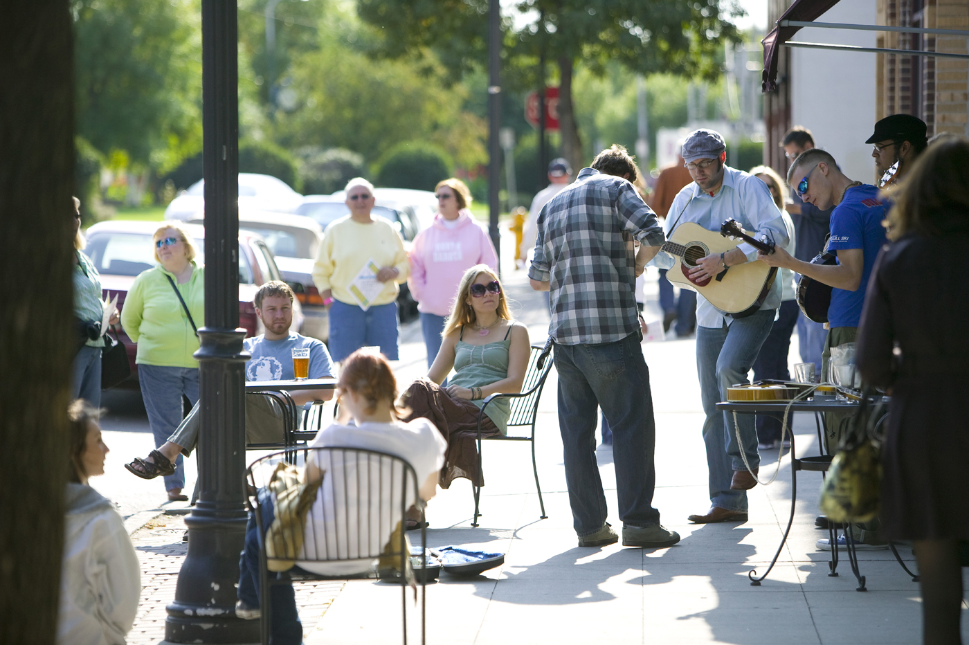 Musicians perform on a sidewalk in Grand Forks as people walk by and sit in chairs.