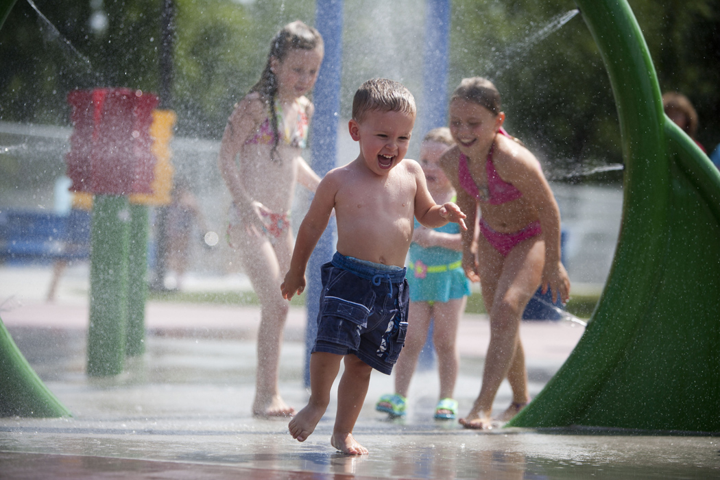 Children play at a splash park in Grand Forks. A little boy laughs as he runs through a water sprinkler.