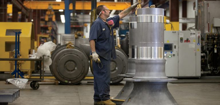 A worker at the Caterpillar Reman plant in Fargo secures a chain to a large metal component shaped like a rocket blaster.