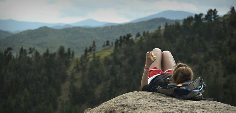 A woman lays down on a cliff overlooking huge mountains and pine trees near Ft. Collins.