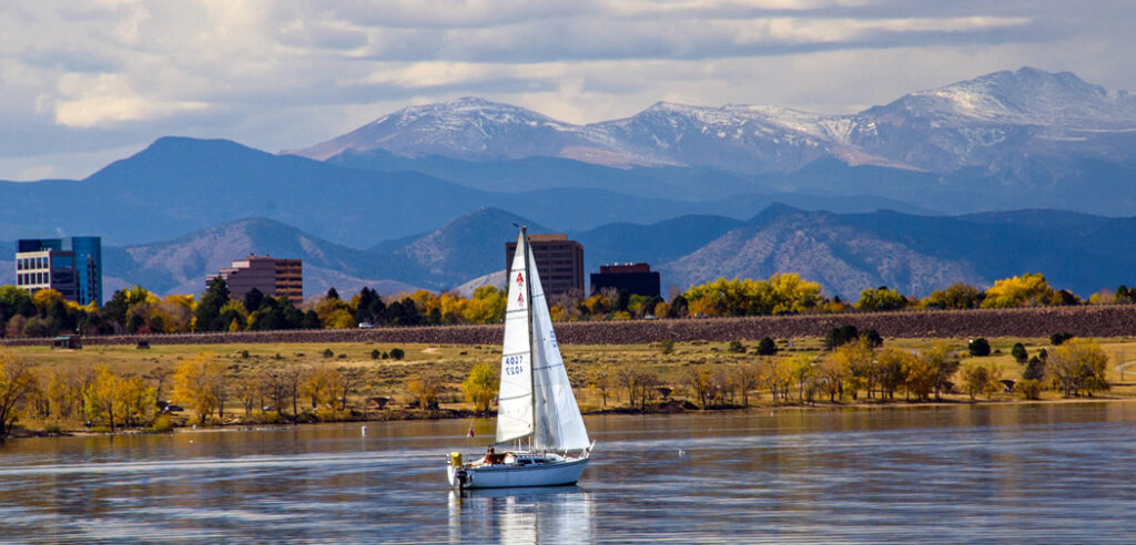 A sailboat floats in front of the skyline of Aurora, CO.