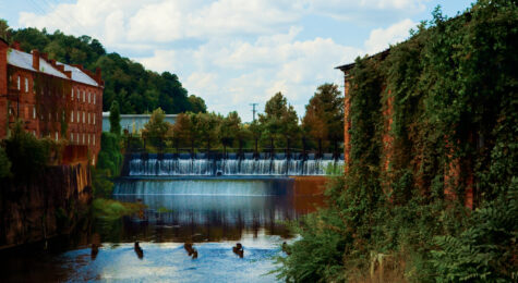 Waters from Autauga Creek flow over a dam in Prattville flanked by an old cotton gin and a brick wall covered in ivy.