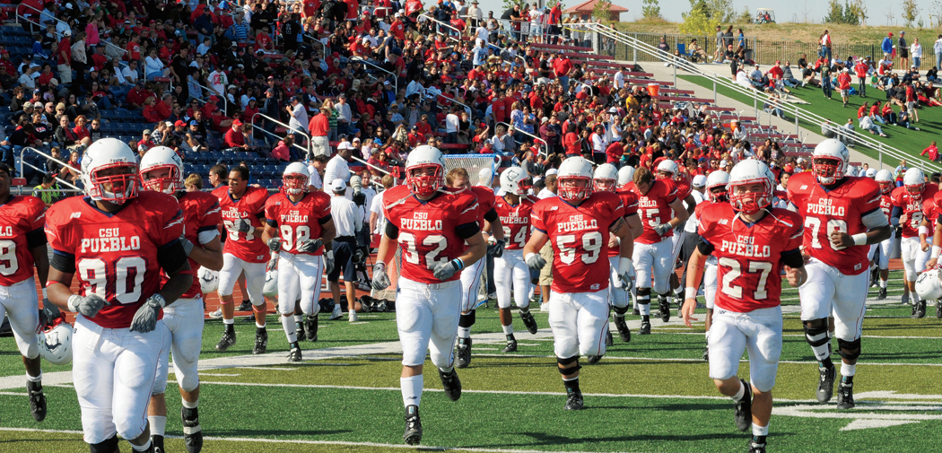 Colorado State University-Pueblo football players take the field in red jerseys and white pants and helmets.