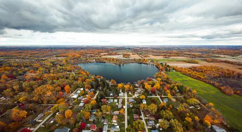 Beautiful full panoramic aerial view of the heart shaped Saugany Lake in Indiana surrounded by residential homes and autumn colored trees or foliage with fluffy white clouds in the sky above