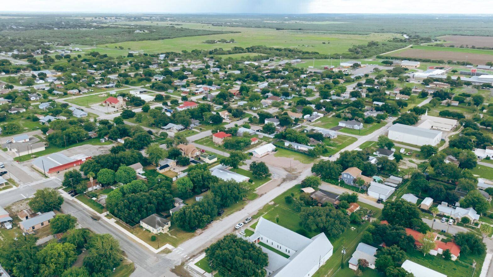 Agriculture agro-town with residential houses, church buildings, small local business surrounding by large farmland ranch in Three Rivers, Texas, suburban rural scene, small town USA, aerial. America