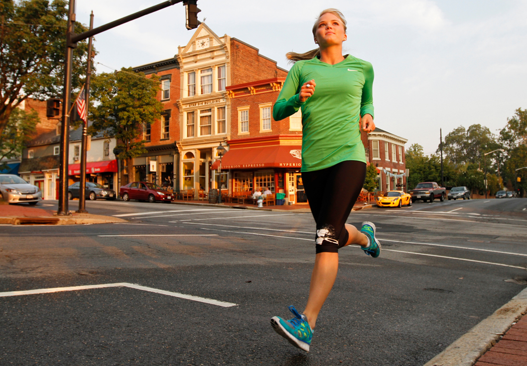 A young woman in a green long-sleeve shirt runs through downtown Fredericksburg, VA.