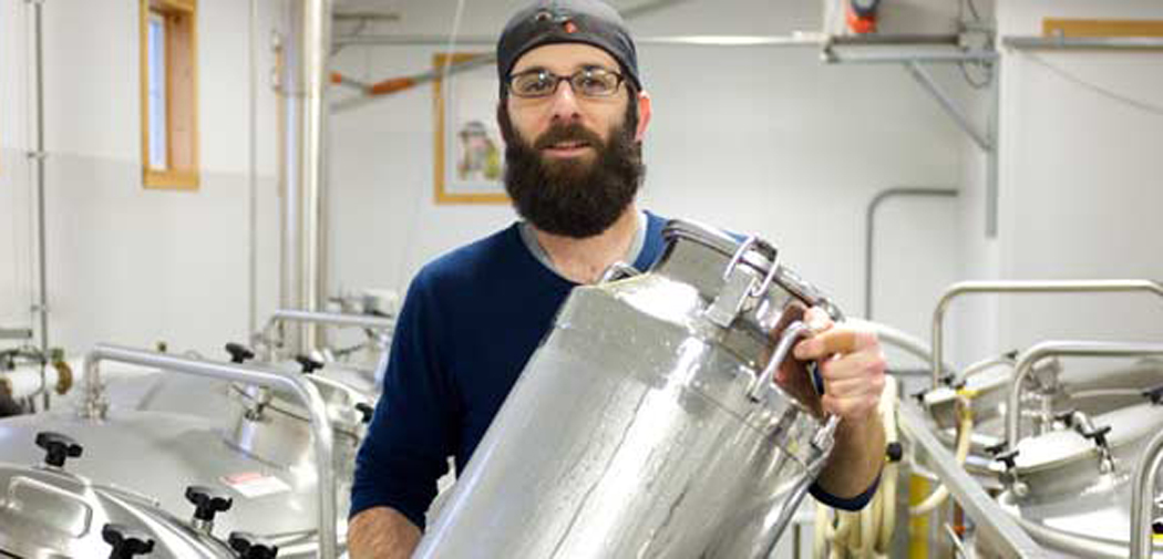 A bearded man holds a keg inside the Main Beer Company.