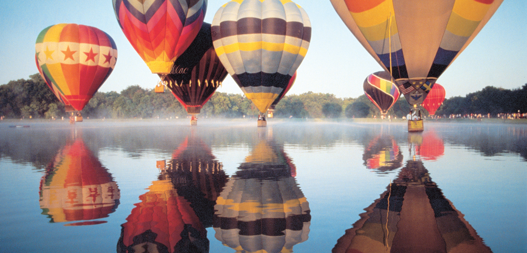 Colorful hot air balloons hover above a lake in Plano, TX.