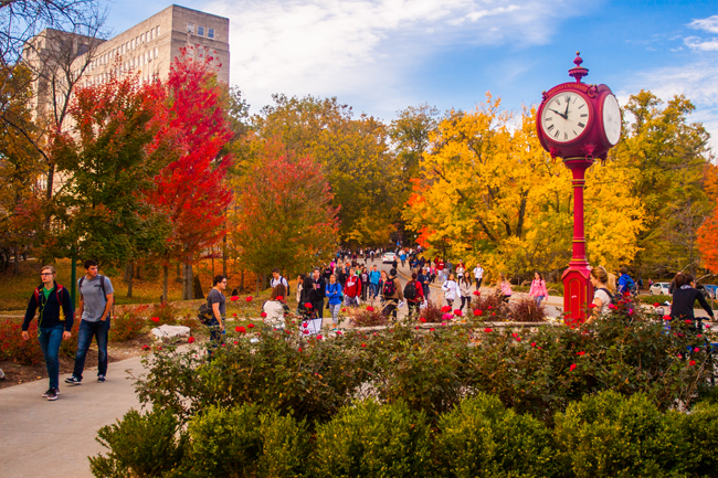 Students walk past brightly colored trees on a fall day at Indiana University