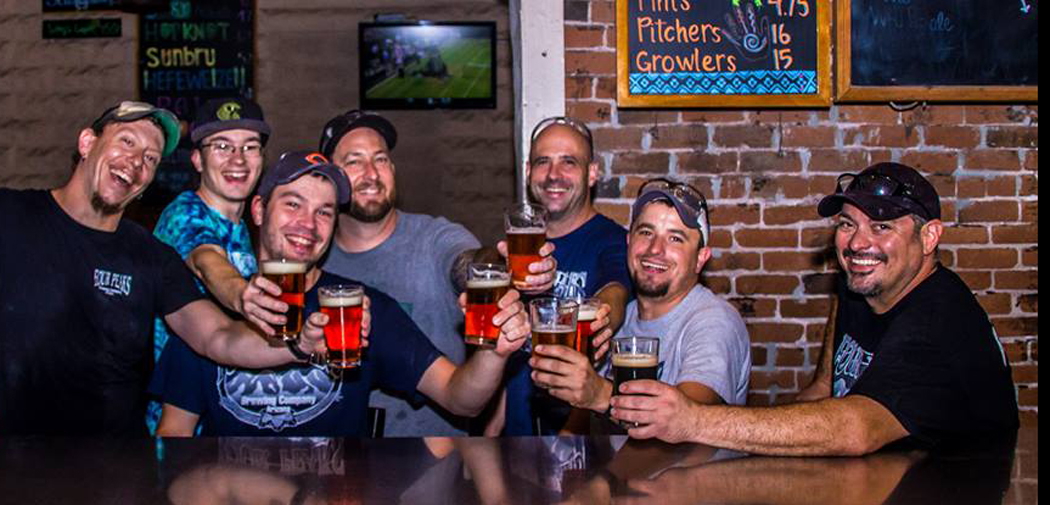 Men hold out pint glasses to toast at Four Peaks Brewing Co.