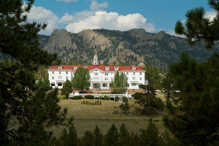 Exterior shot of the Stanley Hotel between the trees in Estes Park CO