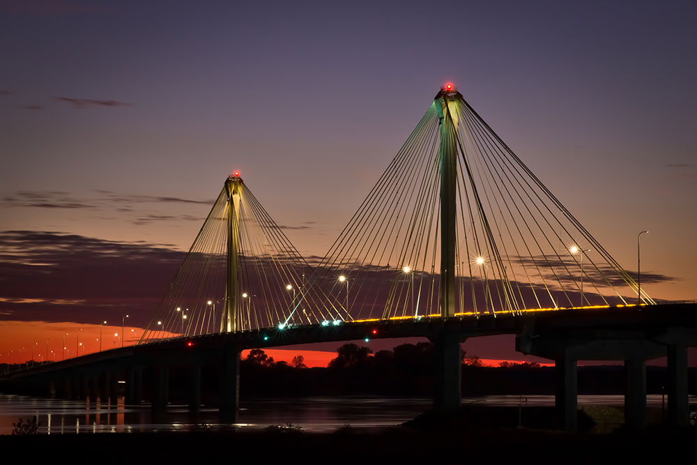 The Clark bridge in Alton, IL silhouetted by a vibrant red and orange sunset. The Clark bridge is a cable stayed bridge that crosses the Mississippi River and connects Alton IL and West Alton, Missouri.