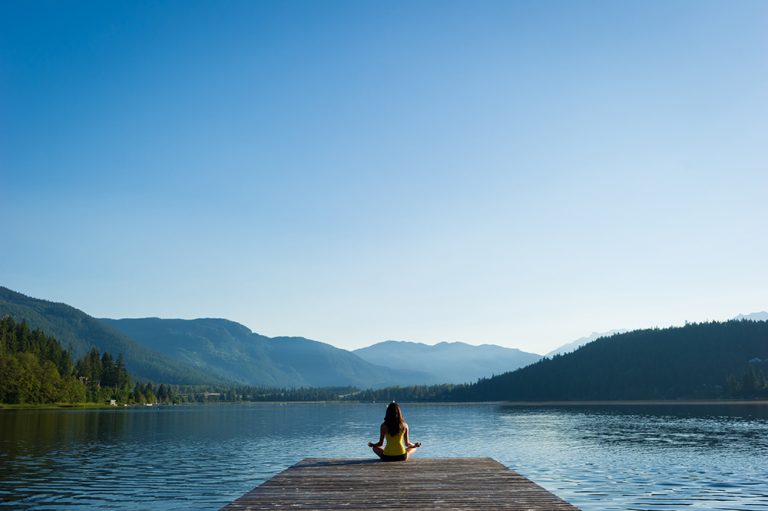 Female doing some soul searching and meditating doing sukhasana or Easy Pose during a yoga working at a pristine mountain lake