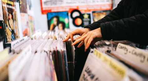 A customer searches through and selects a second hand vinyl record from a shelf in a record store, hands only, horizontal composition. Focus on hands. Close up.