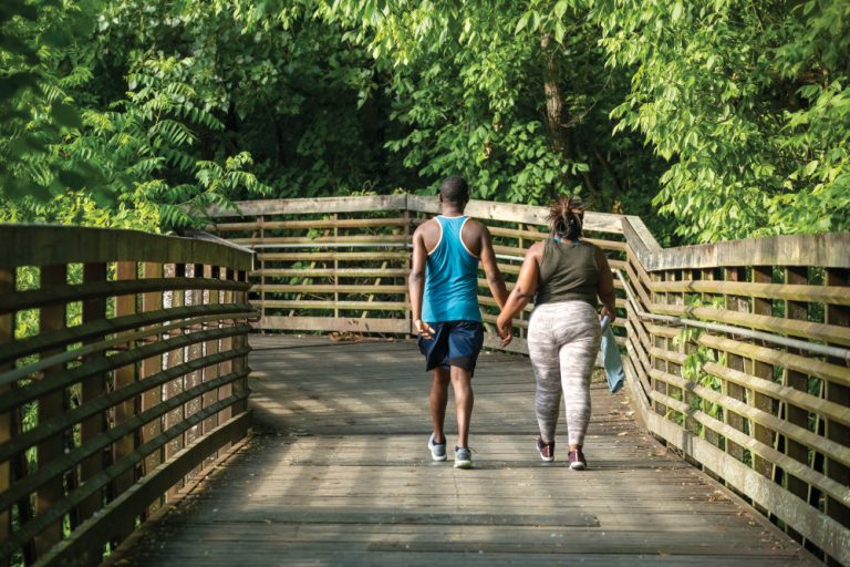A couple walks across a wooden bridge over the West Fork Stones River on the greenway trail in Murfreesboro, Tennessee.