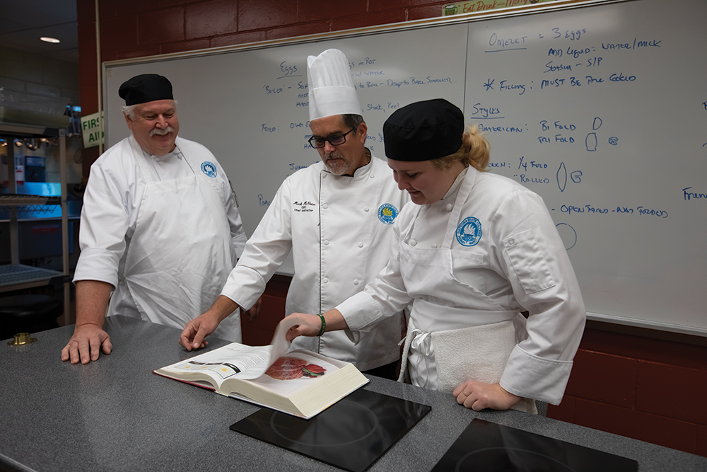 Chef instructor Mark McCann, center, instructs Terry Grubbs, left, and Abigail Killian a classroom at the Mori Hosseini College of Hospitality and Culinary Management on the Daytona State College campus, which is located in the Greater Daytona Region. ©Journal Communications/Nathan Lambrecht