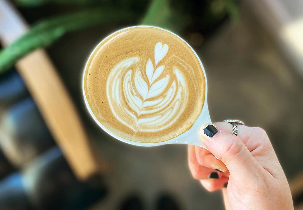 Hand holding a coffee mug, which is filled with a latte from Gold Leaf Coffee Co., located in the Greater Daytona Region of Florida.