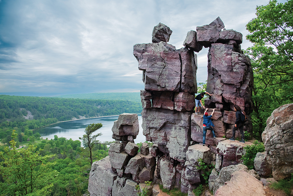 Three friends help each other free climb up to Devil's Doorway. Devil's Lake State Park, Wisconsin, which is located in the Greater Madison Region.
