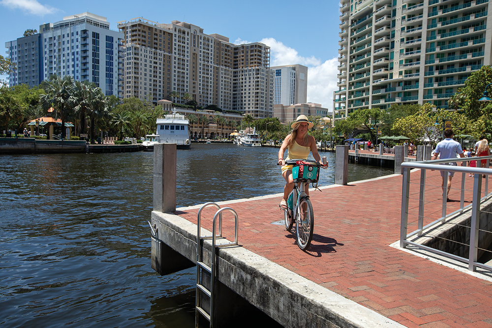 Visitors bike along the New River at Riverwalk Fort Lauderdale in downtown Fort Lauderdale, Florida.