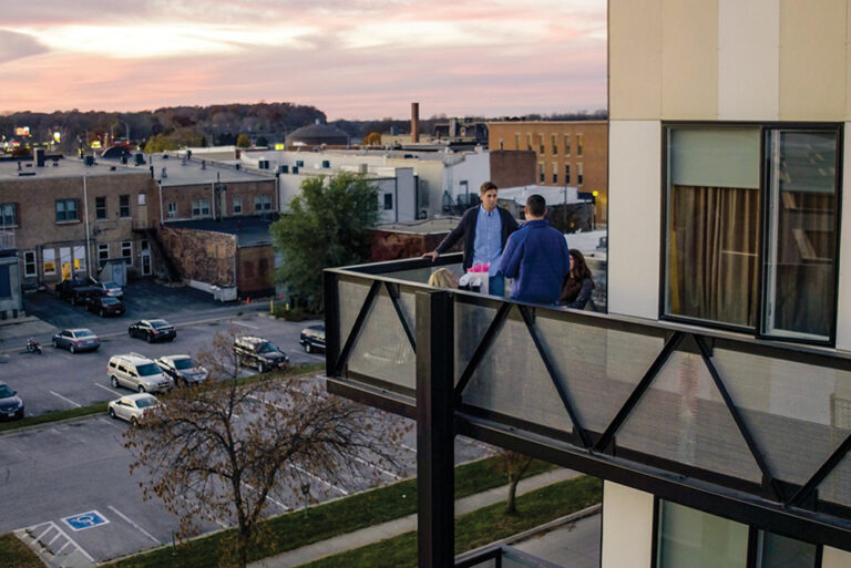 Two men stand outside on a patio at an apartment in the Cedar Valley region of Iowa.