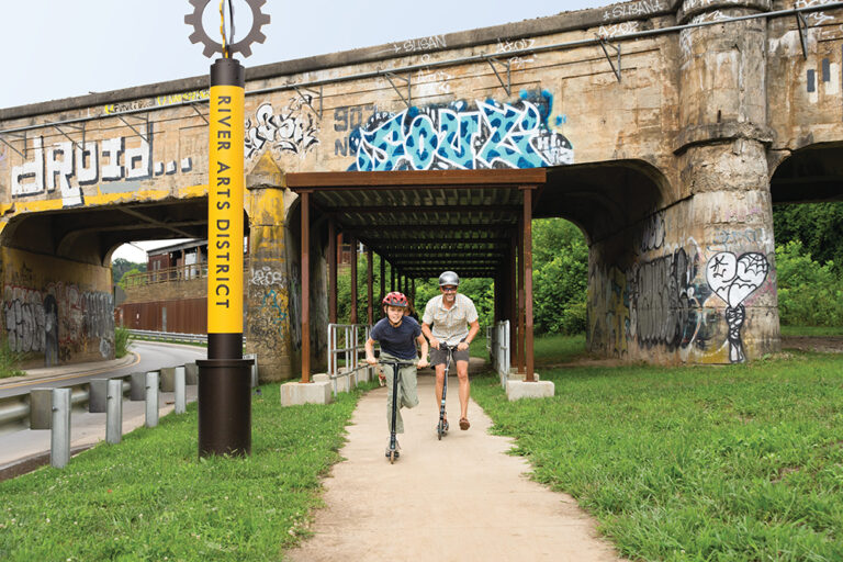 Richard Norris rides his skateboard with his son, Lyndon norris, on the Wilma Dykeman bike path in the River Arts District in Asheville, NC. His wife Denise Marbach Norris walks their dog, Olive, in the background.