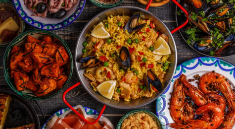 Typical spanish tapas concept. Concept include slices jamon, bowls with olives, anchovies, spicy potatoes, mashed chickpeas, shrimp, calamari, manchego with quince marmalade, pans with tortilla, paella, mussels on a wooden table.