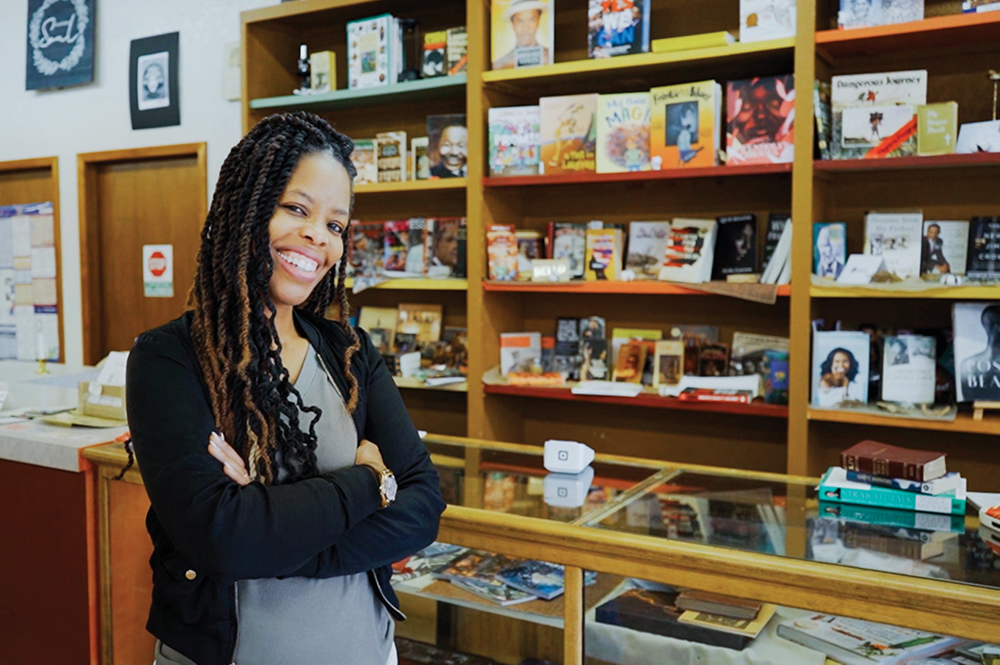 Owner of Soul Book Nook, Amber Collins, stands in front of the counter with books in the background. The bookstore is located in the Cedar Valley region of Iowa.