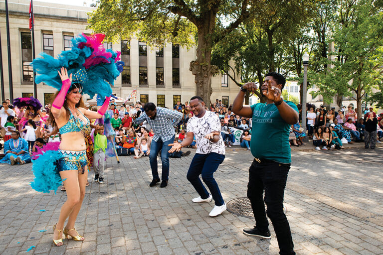 Sam Adelomo, in white, and Isaac Olajide, right, both part of the Nigeria delegation, dance with Siren Dancer Dawn Rhys during a Samba at dance the Jackson International Food and Arts Festival in downtown Jackson, TN.