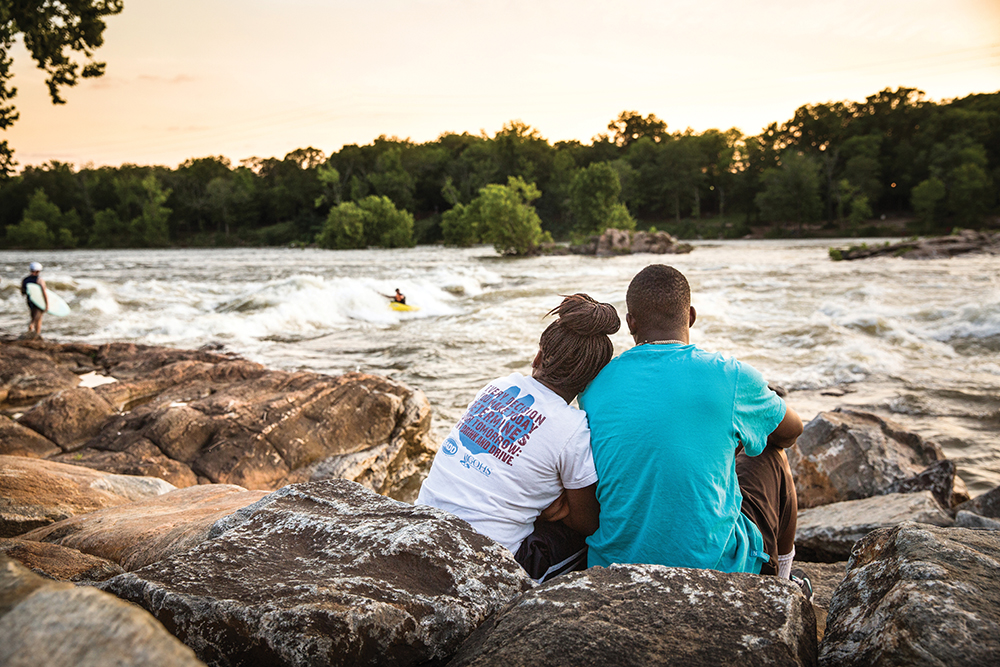 People sitting at a whitewater lookout in Columbus, GA, where visitors can navigate the Chattahoochee River's Class I to Class V rapids on the world’s longest urban whitewater course in the world.