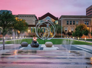 A woman sits in front of a metal sculpture in the square across from the Cedar Rapids Public Library in downtown Cedar Rapids, IA, one of the best places to live in the U.S..