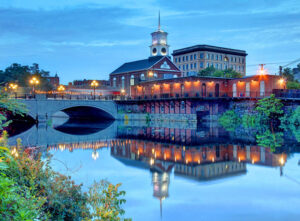A view of Nashua, NH, from the river at dusk. Nashua is a small, eclectic and charming town with beautiful scenery, an affordable cost of living and proximity to Boston and other major metros.