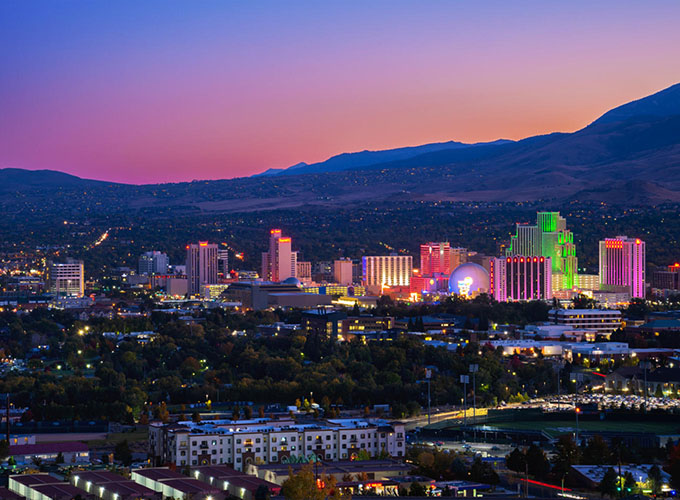 Downtown Reno, NV, skyline at dusk with mountains and a colorful sky. Great public art, a craft beer scene, a bustling riverwalk and beautiful scenery with premier access to outdoor activities make Reno one of the best places to live in the U.S.
