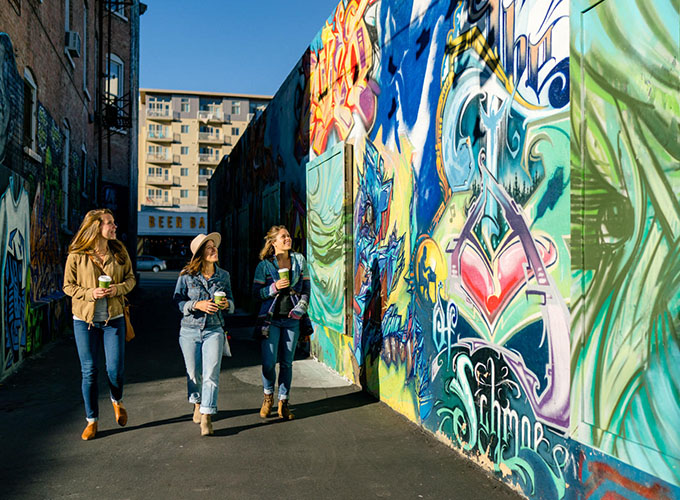 Women walk past a colorful mural in Salt Lake City, UT. Utah’s capital city has a robust transportation system, an international airport and a thriving arts scene.