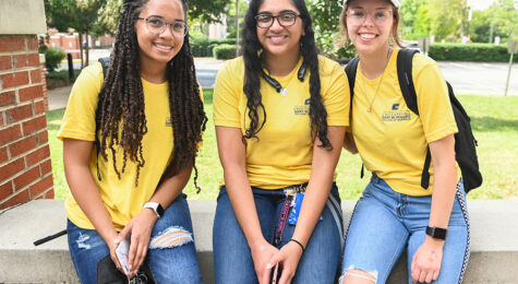 Three female students pose for a photo in front of Fletcher Hall, home of the Gary W. Rollins College of Business.