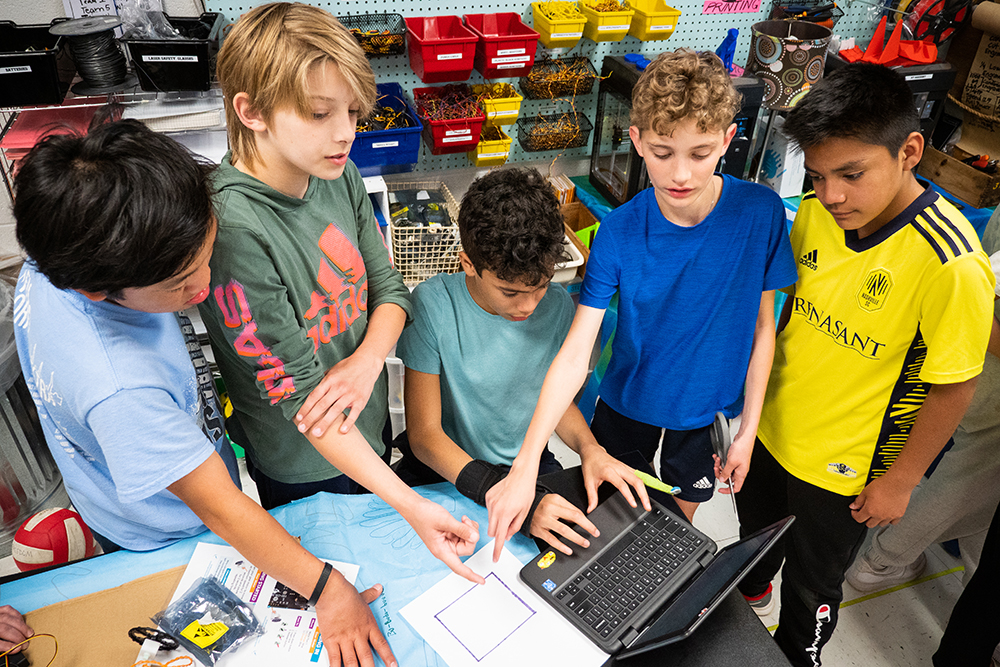 A group of young male FSSD students congregate around a computer to collaborate on a project.