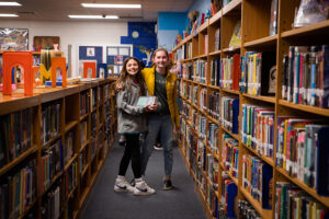 Two female FSSD students smile for a photo in the library.