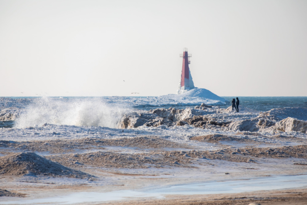 Visitors are surrounded by crashing waves on the sand dunes along the shore of Lake Michigan near the South Breakwater LIghthouse at Pere Marquette Park along Lake Michigan in Muskegon, Michigan.