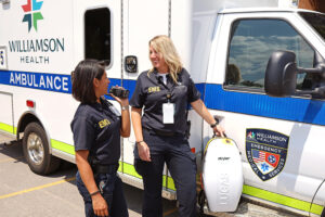 Two Williamson Health EMS responders stand in front of an ambulance.