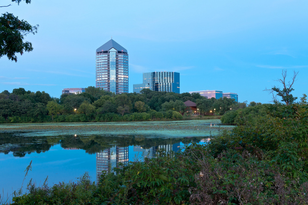 High-rises in downtown Bloomington, MN, are visible beyond Mount Normandale Lake. Bloomington is a best place to live in Minnesota.