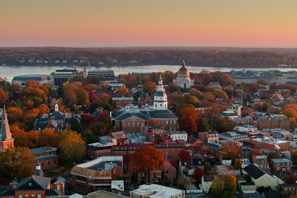 Aerial shot of Annapolis at sunrise on a hazy morning in the Fall, looking past the dome of the Maryland State House towards the campus of the US Naval Academy, with the Chesapeake Bay beyond. Annapolis is one of the best cities to live in Maryland.
