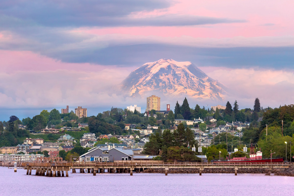 Mount Rainier rises from the clouds beyond a waterfront view of Tacoma, Washington, at sunset. 